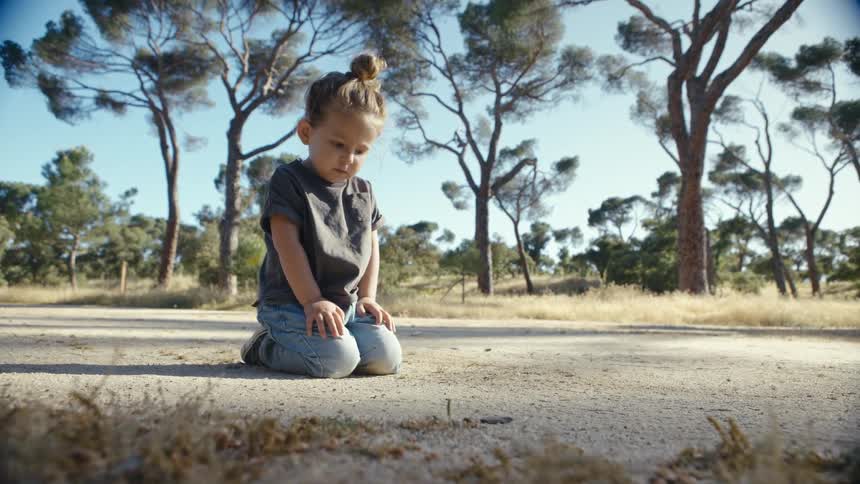 Child kneeling on dirt path among trees