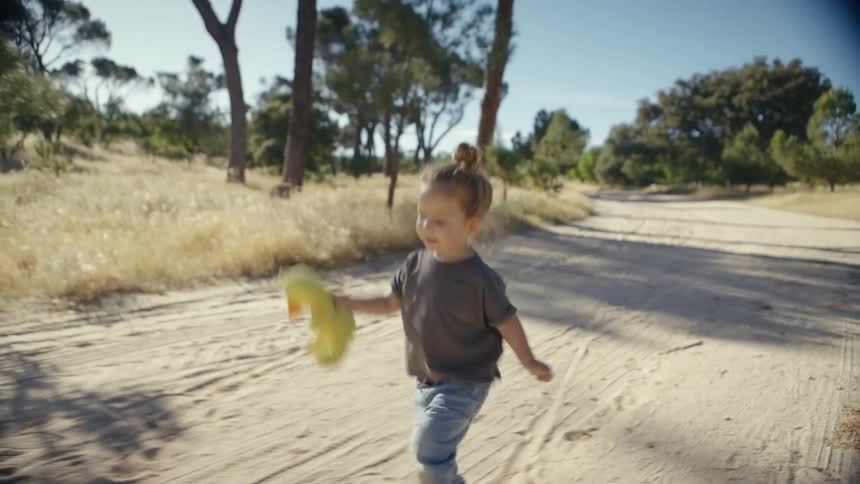 Smiling little girl holding a stuffed animal and running along an outdoor trail