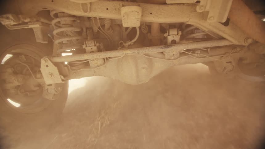 View from under a jeep traveling on a dirt road as dust flies