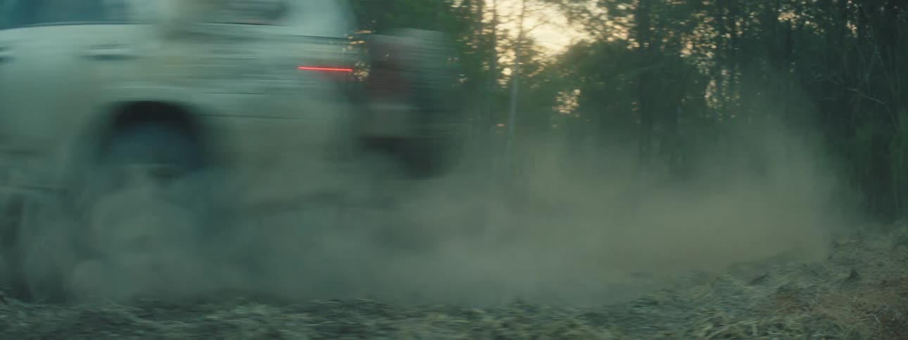 Pickup truck with headlights on taking a turn on a trail and kicking up dust