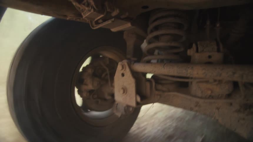 Underside of a vehicle showing a wheel moving through mud