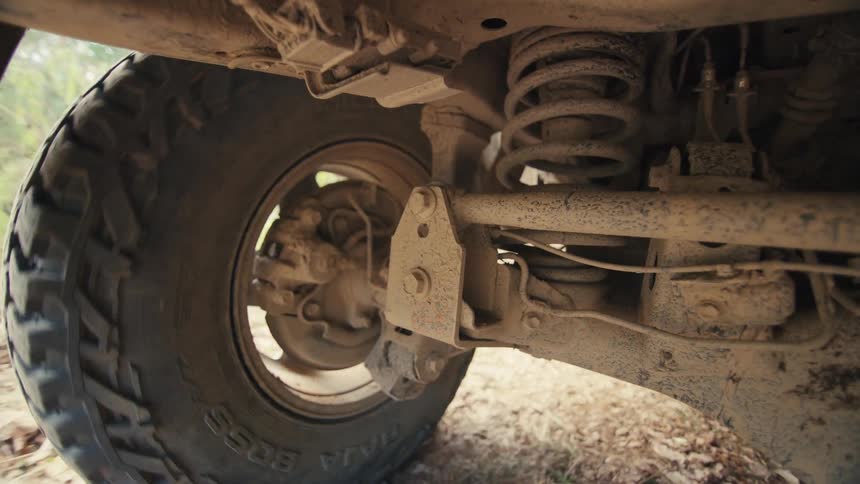 View from under a jeep traveling on a dirt road as the wheel turns and the spring moves