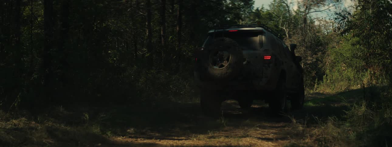Mudcovered sport utility vehicle drives along a dirt trail in a forest area