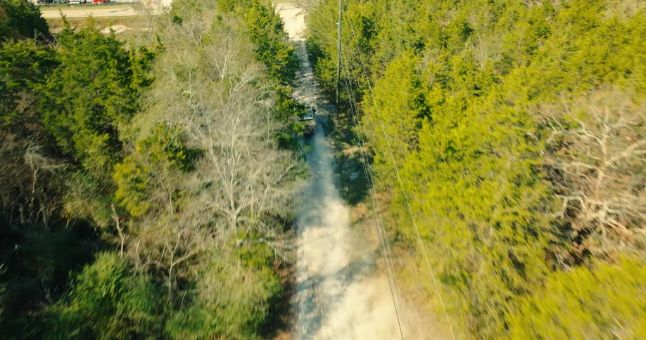 Aerial view of a pickup truck kicking up dust on a forest trail