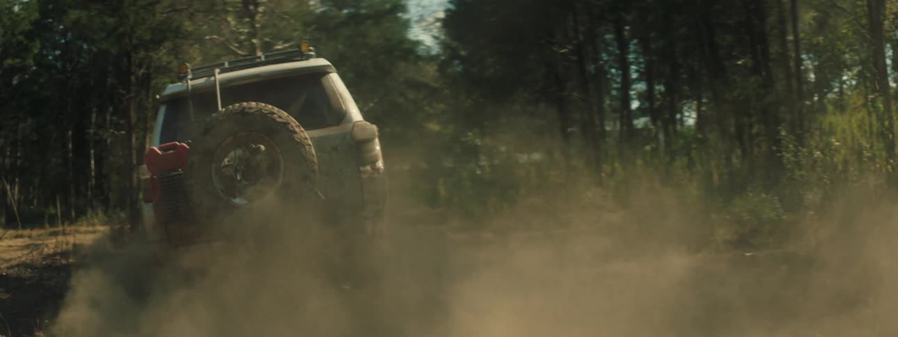 Truck travels on a rural dirt road in the woods leaving behind a trail of smoke and dust