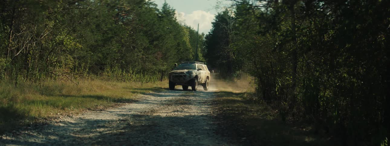 Suv drives along a dirt road between trees raising dust