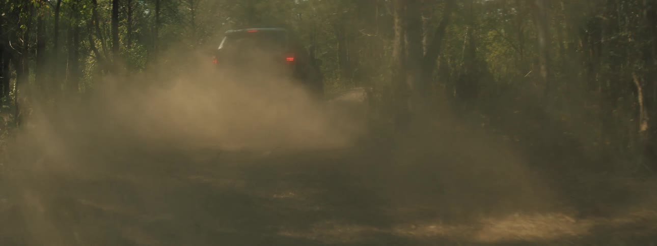 An offroad suv speeds down a narrow dirt trail through a dense forest a thick cloud of dust billows from behind the vehicle as it disappears into the trees