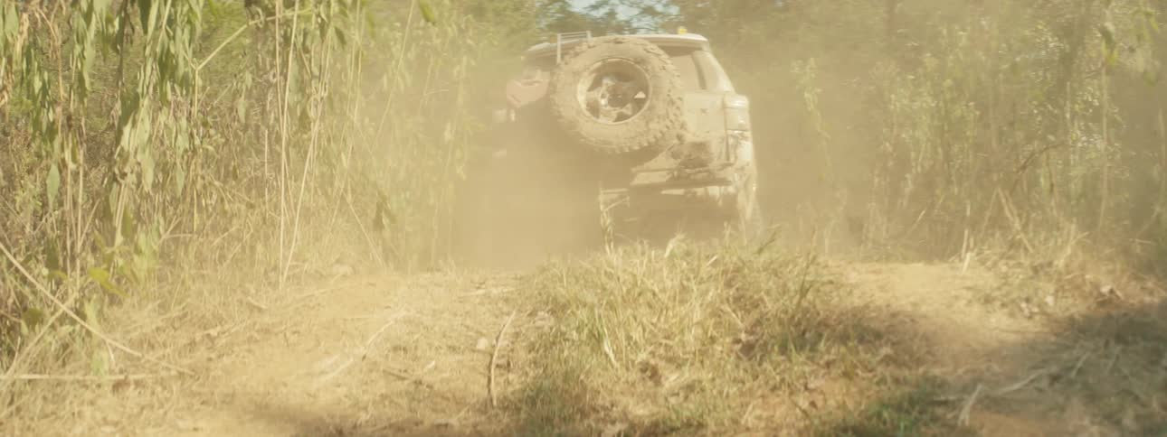 A rugged offroad vehicle kicks up a massive cloud of dust while navigating a narrow wooded trail the suv continues its journey through the dense brush equipped with a roof rack and a spare tire on the back