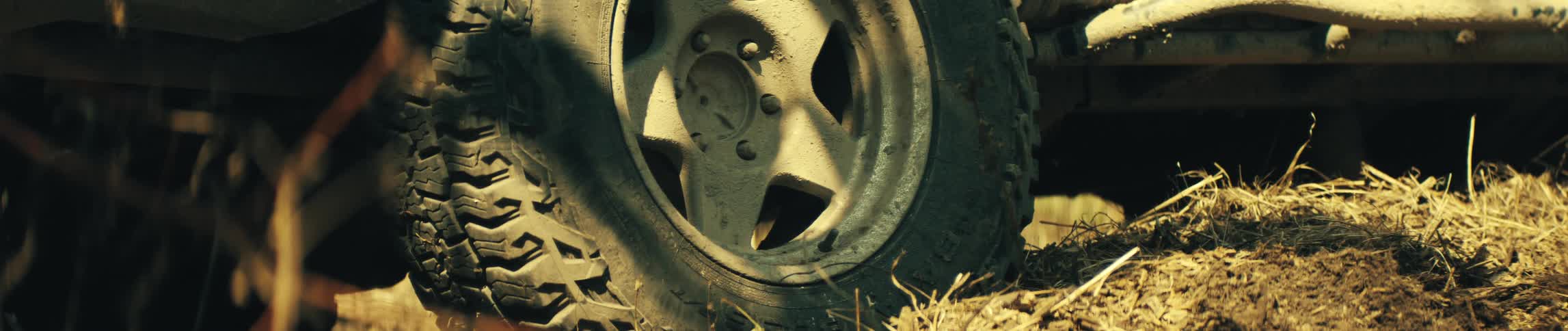 A close view shows a stationary tire and rim covered in dried tan mud while sitting on dry grass