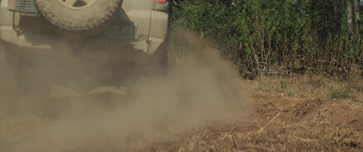 An offroad suv driving through the woods at midday covered in dust