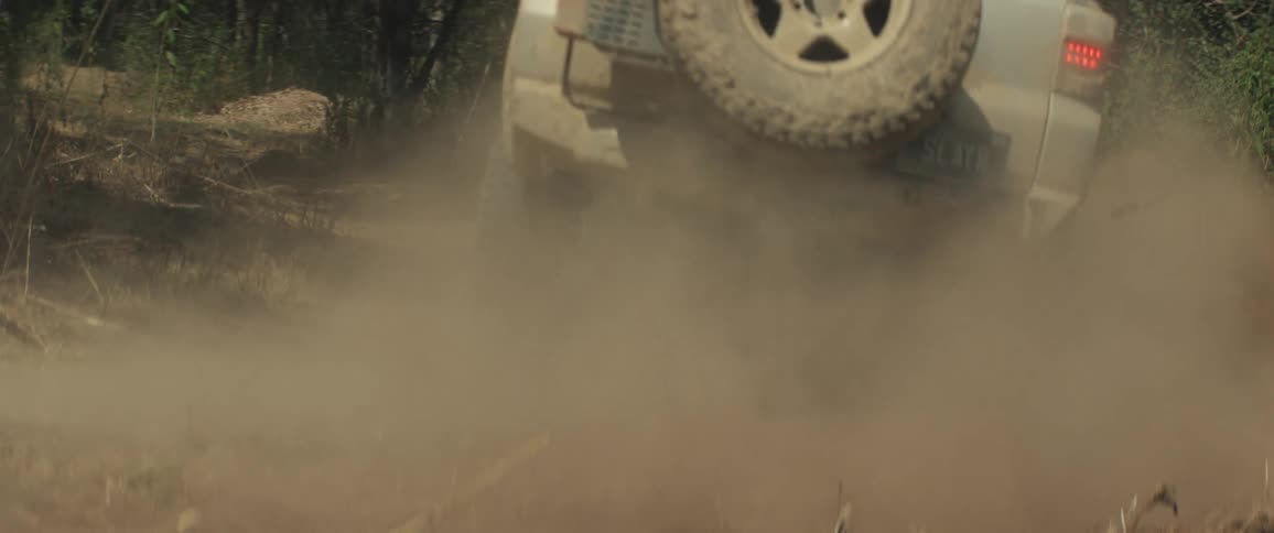 Rear of suv raises dust while moving along a dirt trail in a forest area