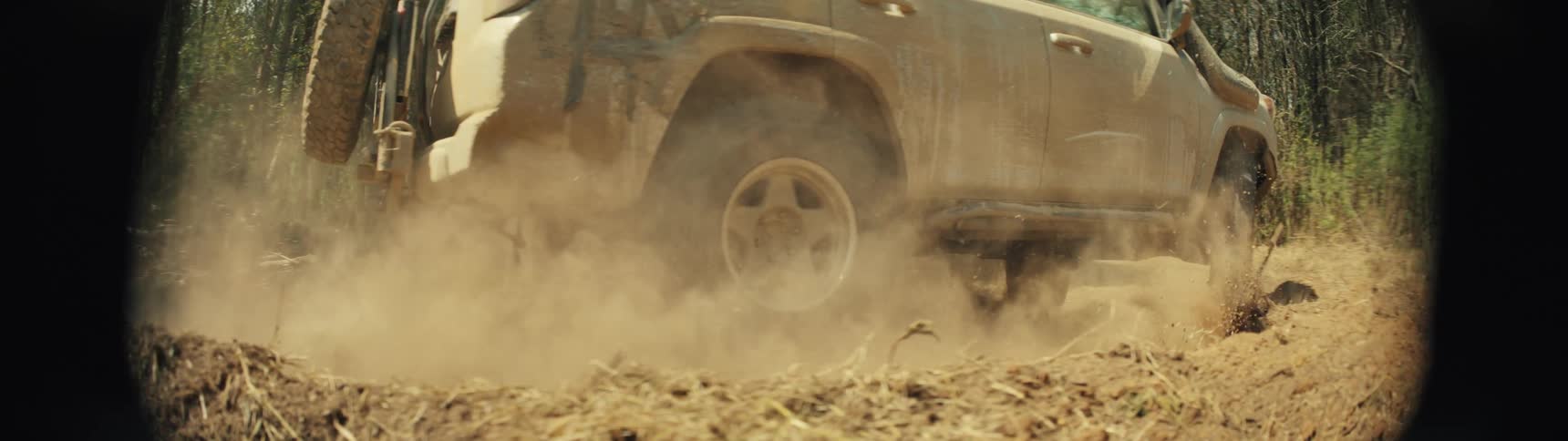 Mudcovered suv drives along a dirt trail raising dust among trees
