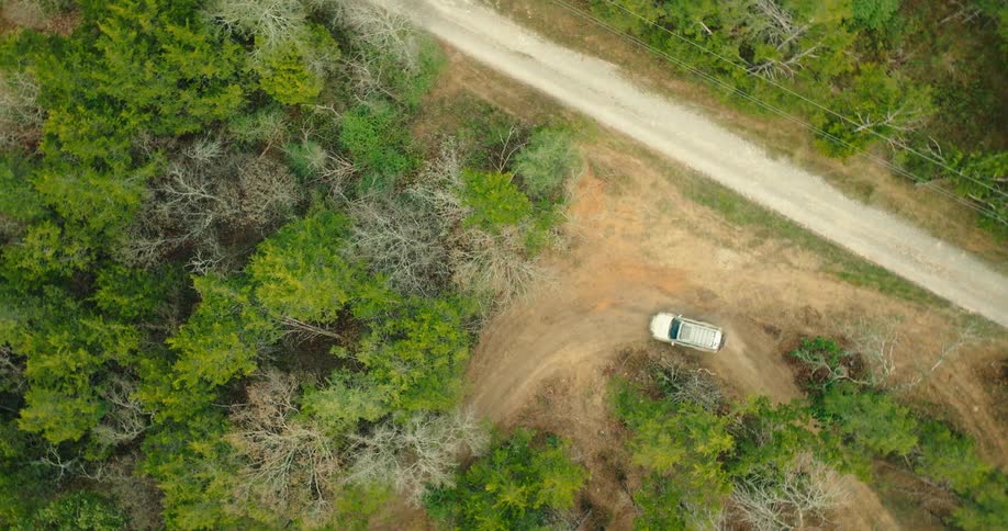 White suv drives along a curved dirt road surrounded by trees seen from above