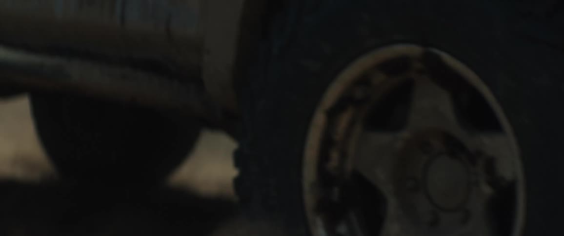 A heavy truck driving across a field at sunset with large tires rolling over the sand and kicking up dust behind it