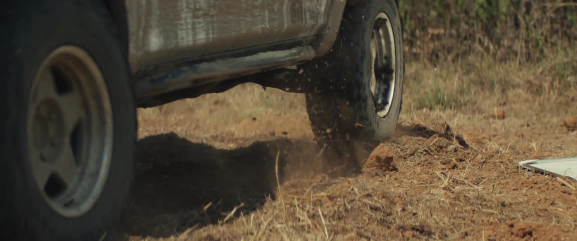 Rear wheels of a sport utility vehicle kick up dust while driving on a dirt road