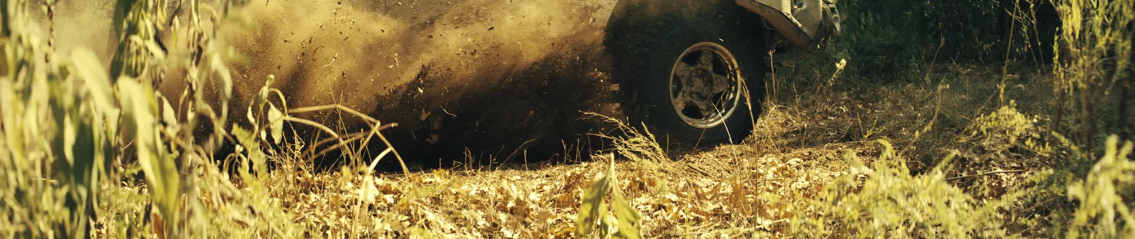 Dust and dirt fly into the air behind a jeep as it travels through dry plants and vegetation in the wilderness