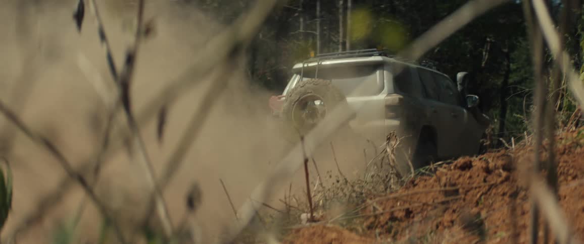 Dustcovered sport utility vehicle drives along a dirt road between trees