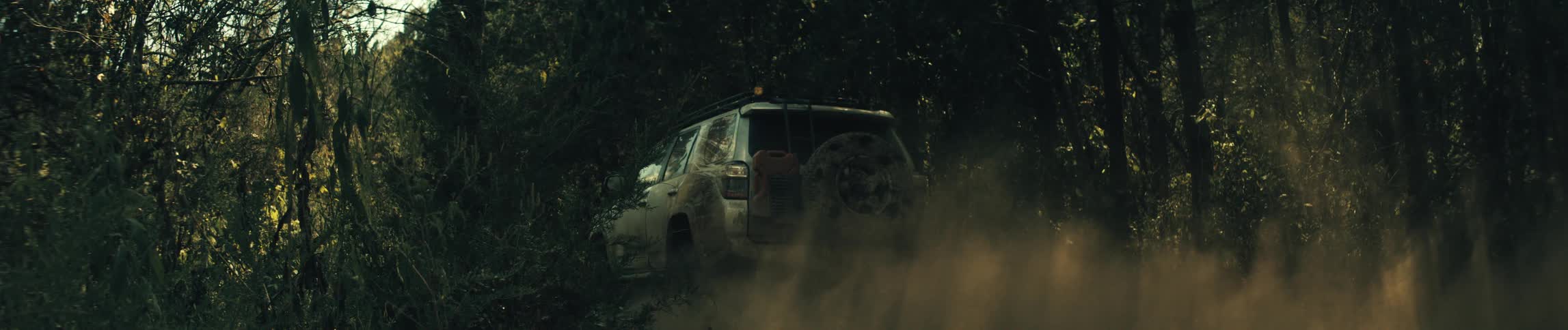 Mudcovered suv travels along a narrow trail between trees raising dust