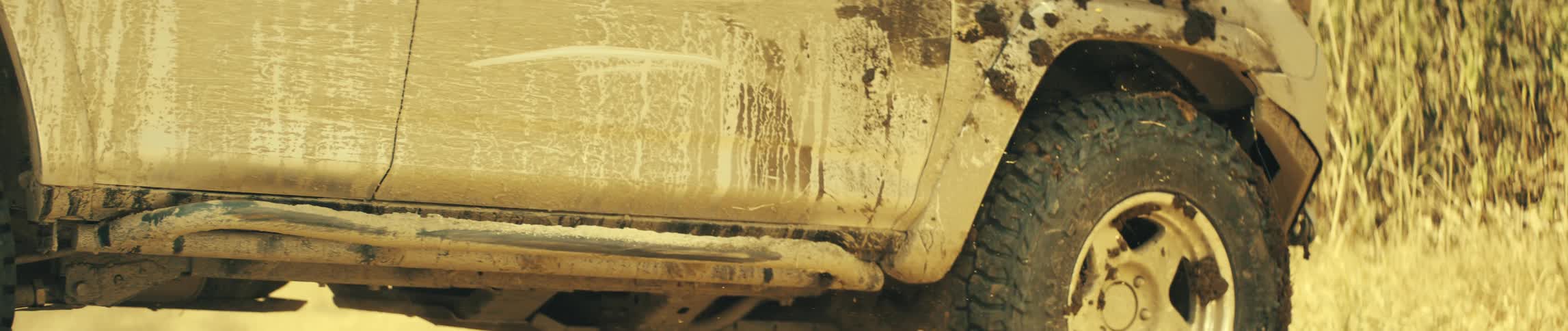 Underside of a mudcovered suv passes over dirt terrain raising dust