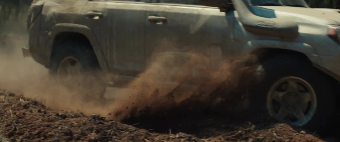 Smoke and dust fill the air as a truck travels on a dirt road through the woods
