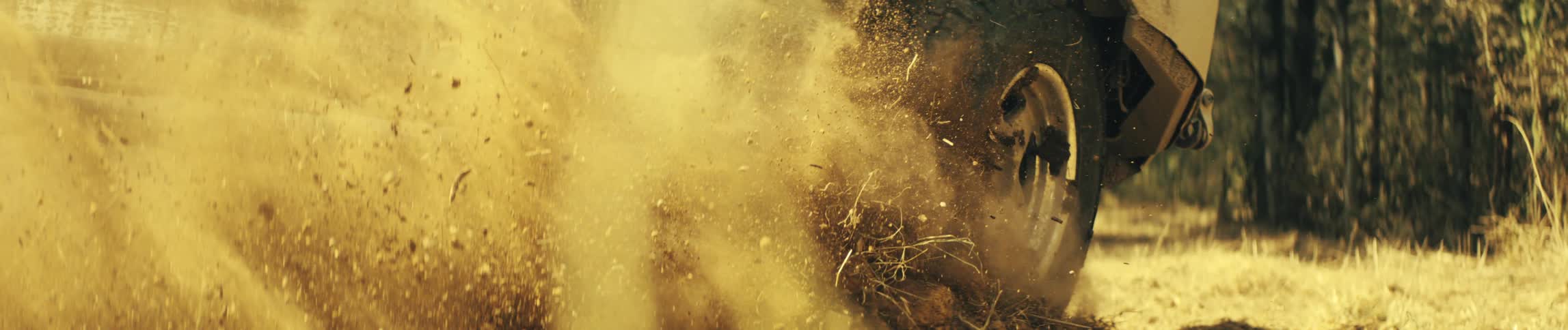 A close ground level view shows a large tire spinning and kicking up dirt and dry straw as the vehicle drives forward