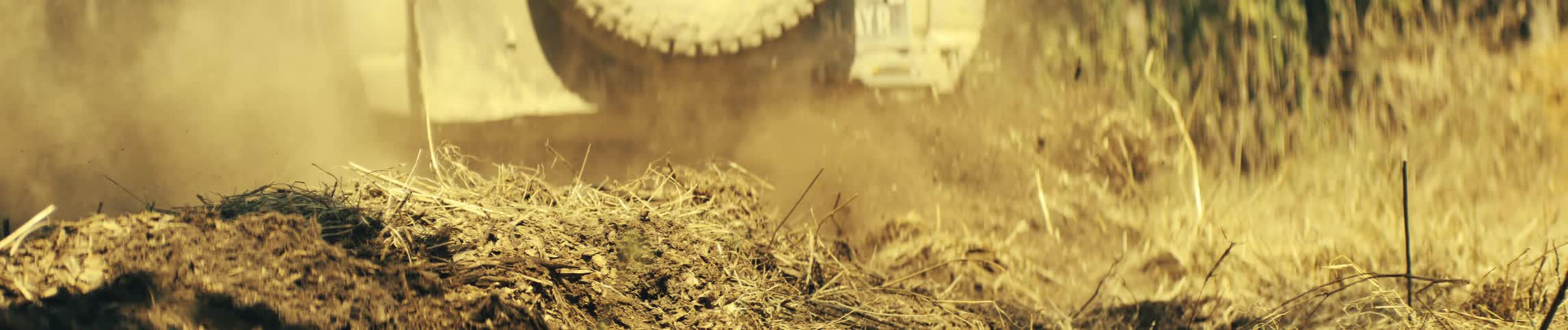 Dirt flies behind a jeep as it moves though dry vegetation on the ground