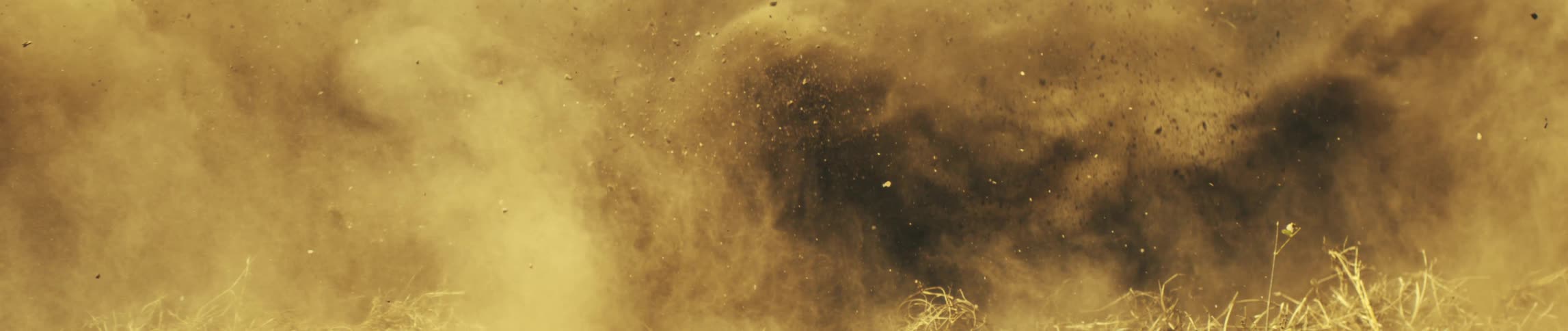A suv vehicle passes by dry ground and sends a massive cloud of brown dust and dark earth upward filling the frame with swirling silt flying pebbles and scattered bits of hay