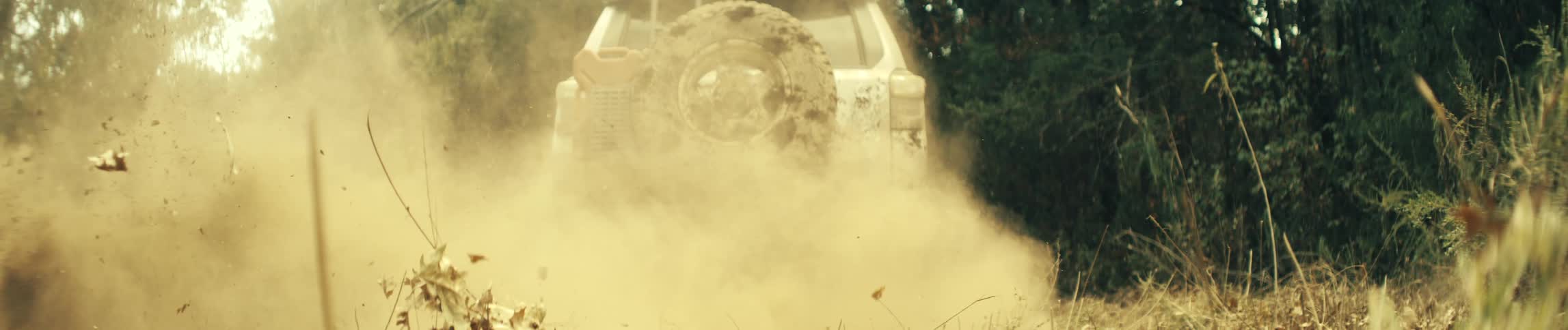 Truck turns on a rural dirt road in the woods as smoke and dust fill the air