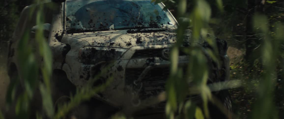 An offroad vehicle driving through a forest with dust blowing up behind it at midday