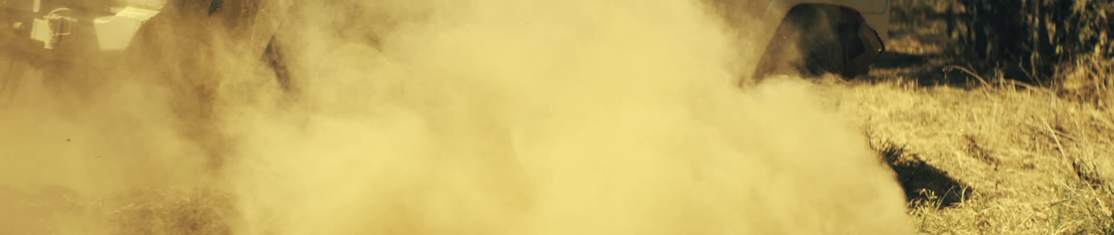 An offroad suv driving through the woods at midday leaving a cloud of dust behind