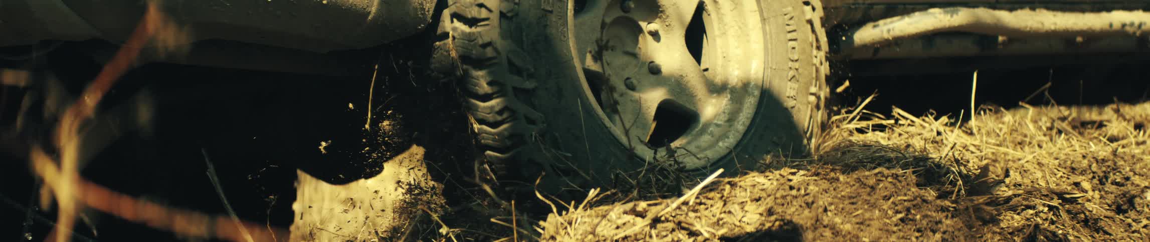 Vehicle wheel moves across ground with dirt and dry vegetation