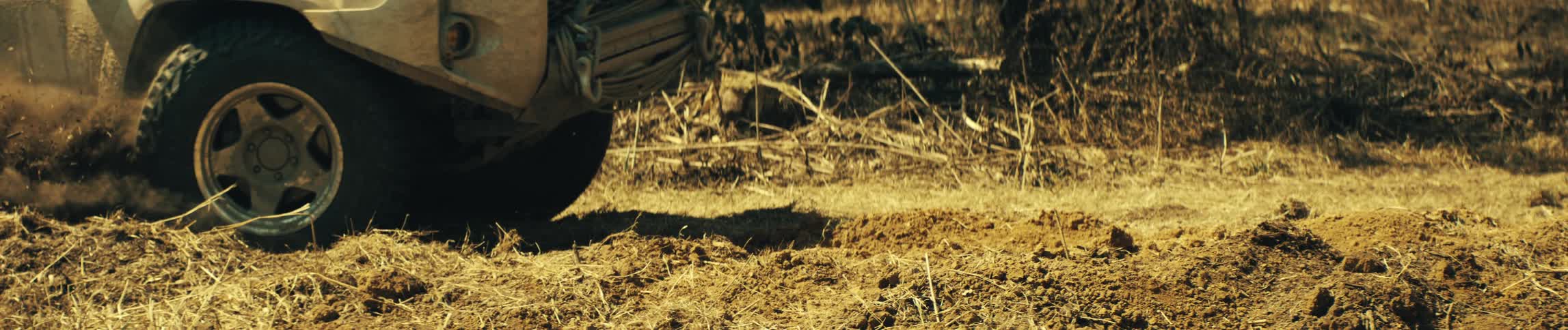 Suv wheel spins on a dirt road kicking up dust and debris