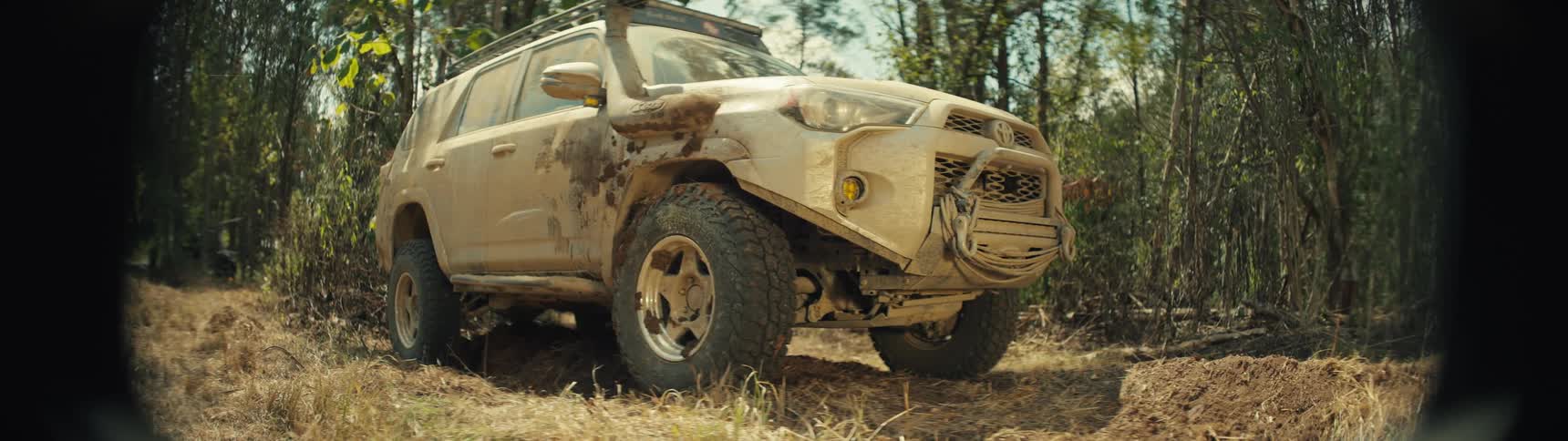 Mudcovered suv moves along an uneven dirt trail in a forest area