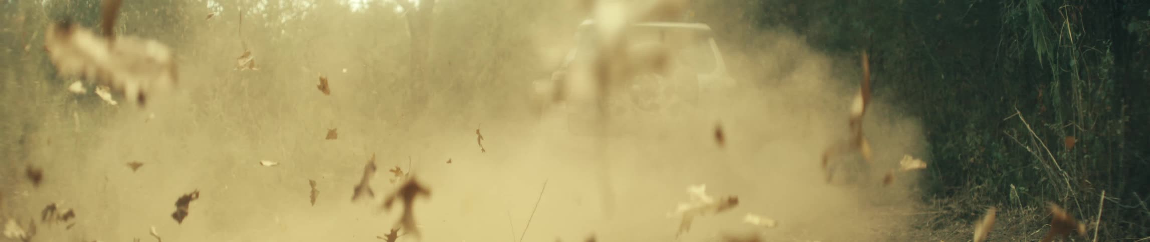 A close ground level view shows the front wheels of a mud covered vehicle spinning and kicking up dirt and dry leaves as it drives forward