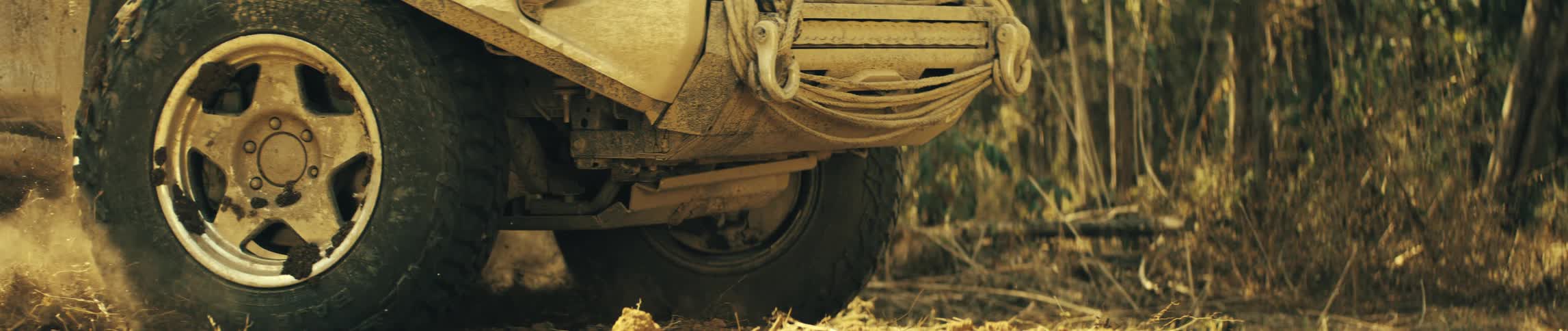 An offroad vehicle driving through the forest kicking up dust behind it at midday