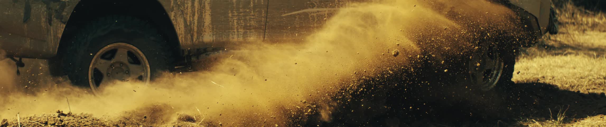 An offroad suv driving through the sand spraying dust behind it at midday