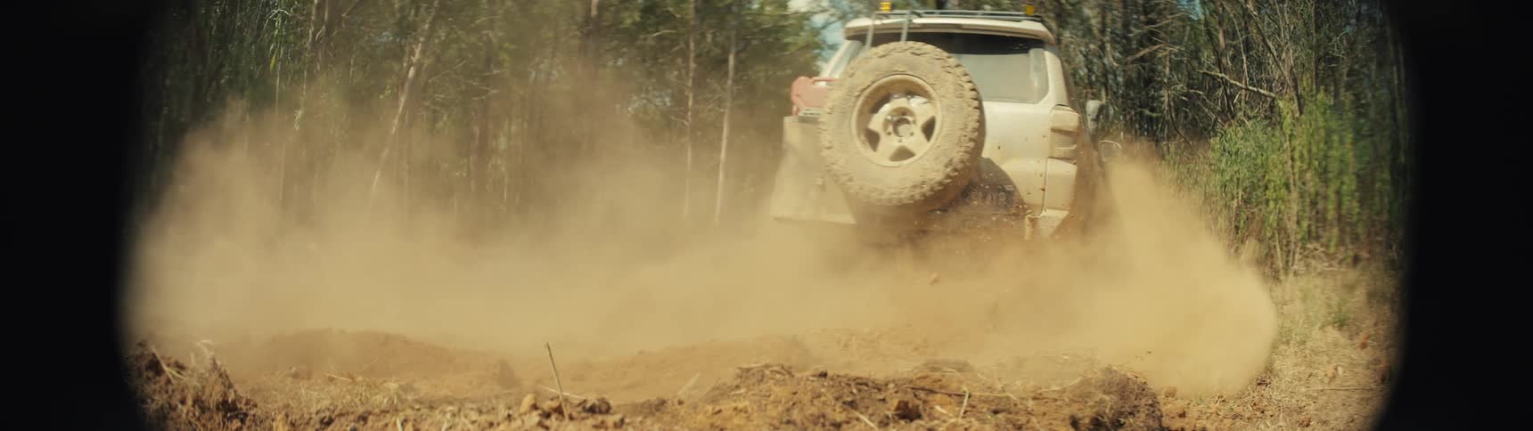 An offroad suv driving on a dirt road in the forest blowing dust behind it at midday