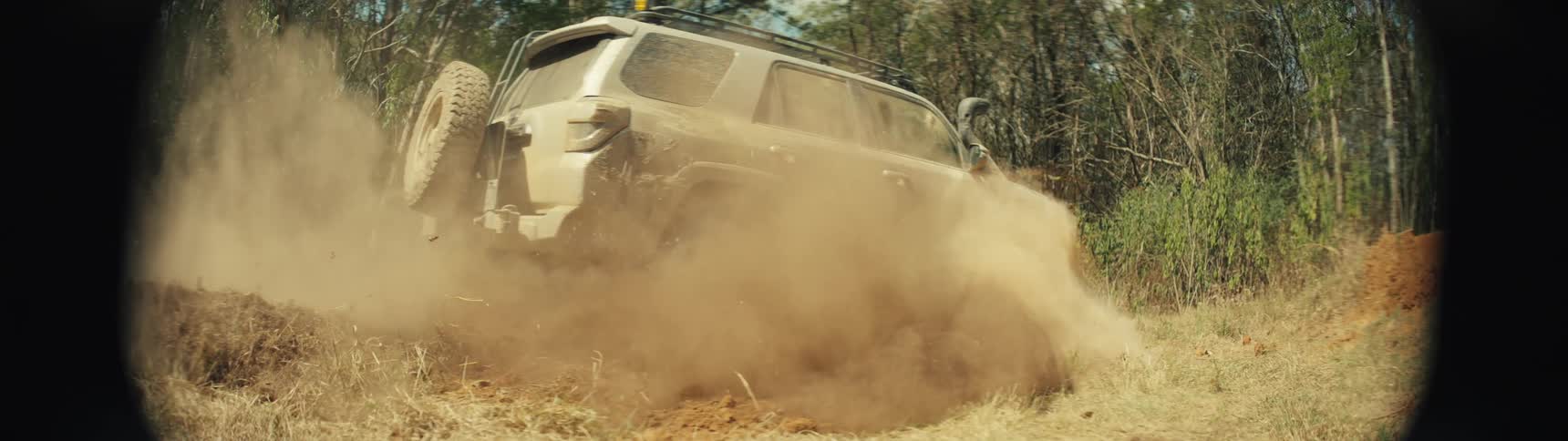 An offroad vehicle driving through a forest on a sunny day kicking up dust behind it