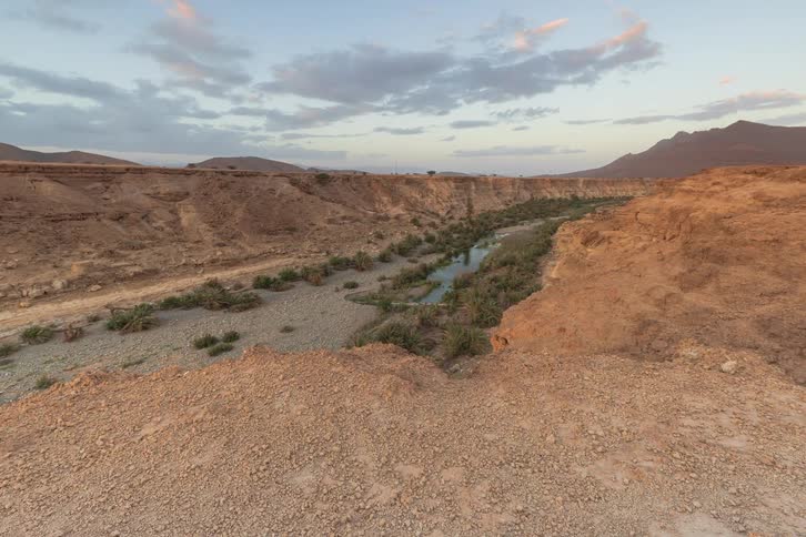 A time lapse shot captures the changing light over a desert canyon with a winding stream at sunset