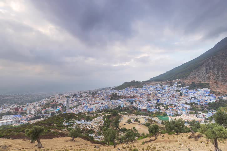City with blue houses spread across a mountainside under a cloudy sky