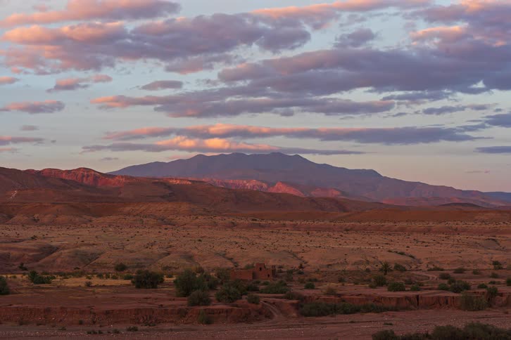 Automobiles move on desert roads with red rock mountains across the landscape under a cloudy sky