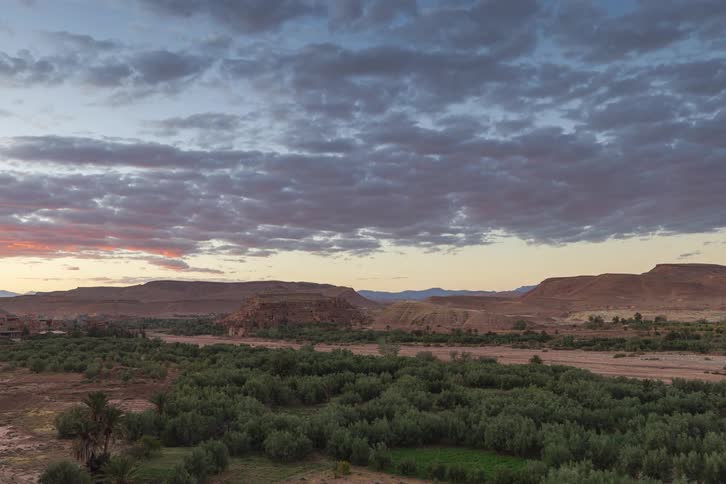 Under a vast sky of textured clouds a quiet desert valley stretches across the horizon blending rugged mesas with pockets of green life