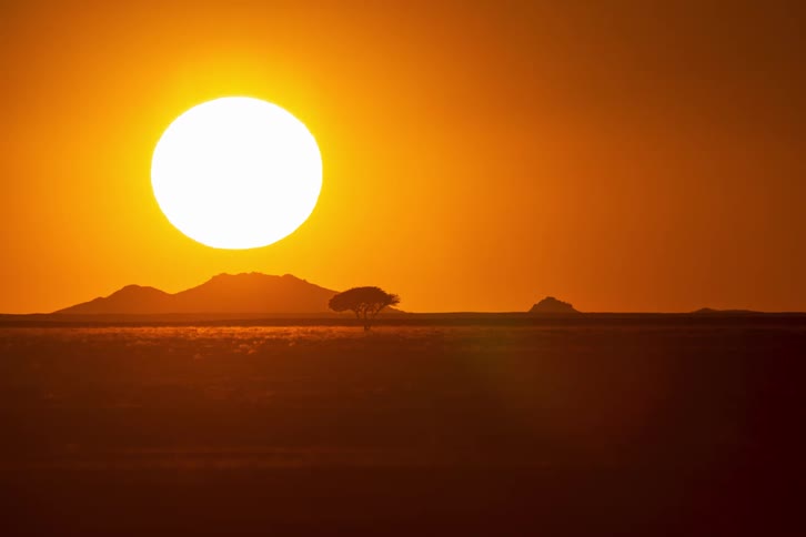 Sun sets over mountains in a deep orange sky