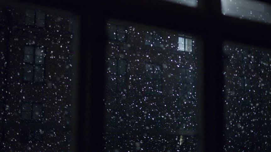 Snow falls past outside the window at night