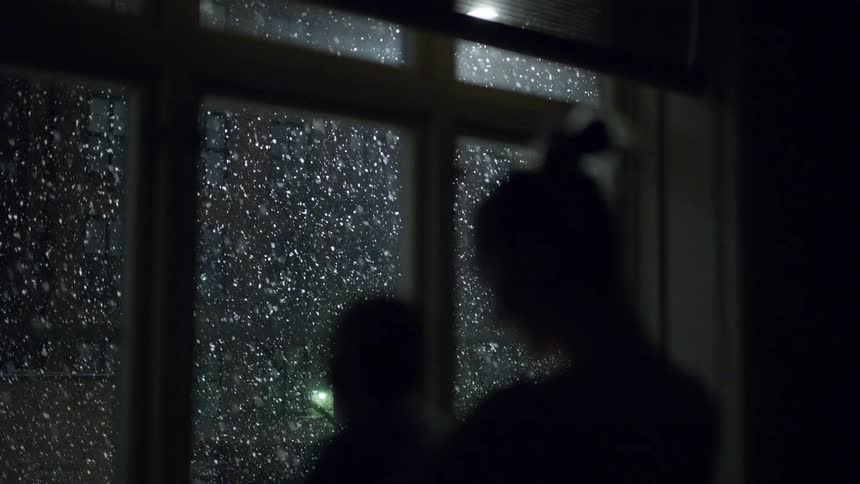 Woman standing in front of windows with her young child watching snow fall