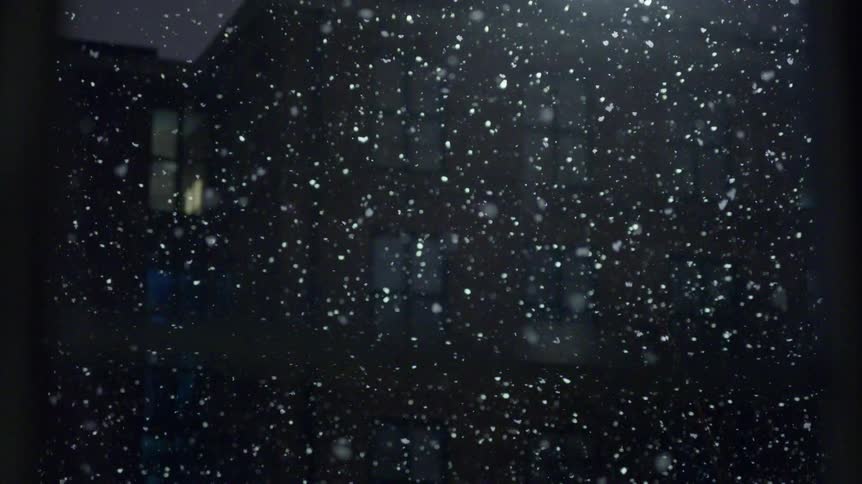 View through windows of snow falling on the neighborhood illuminated by a streetlight