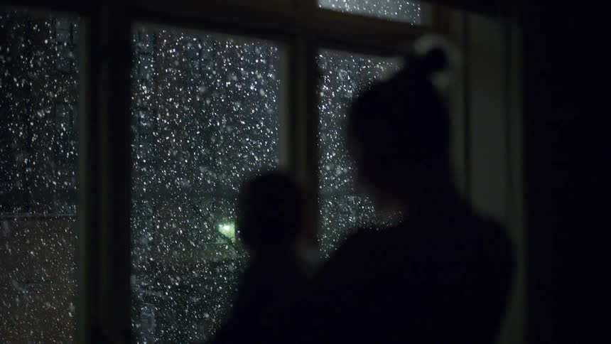 Mother holds her baby while staring out the window at a snowy night