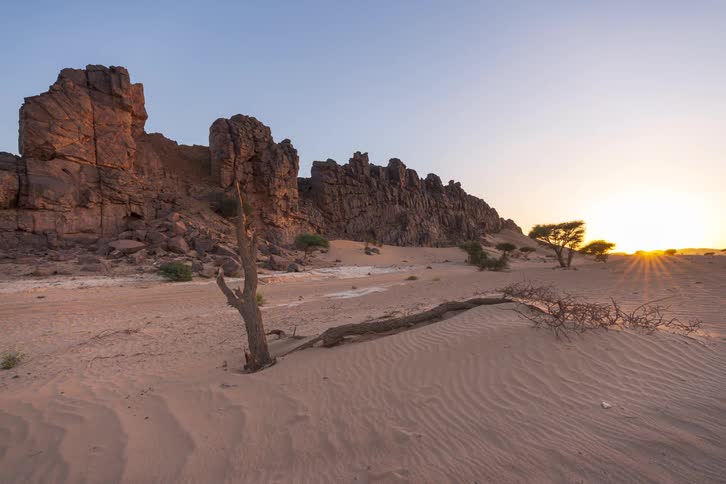 Rock formations and sand dunes illuminated by the sun at sunset in a desert landscape