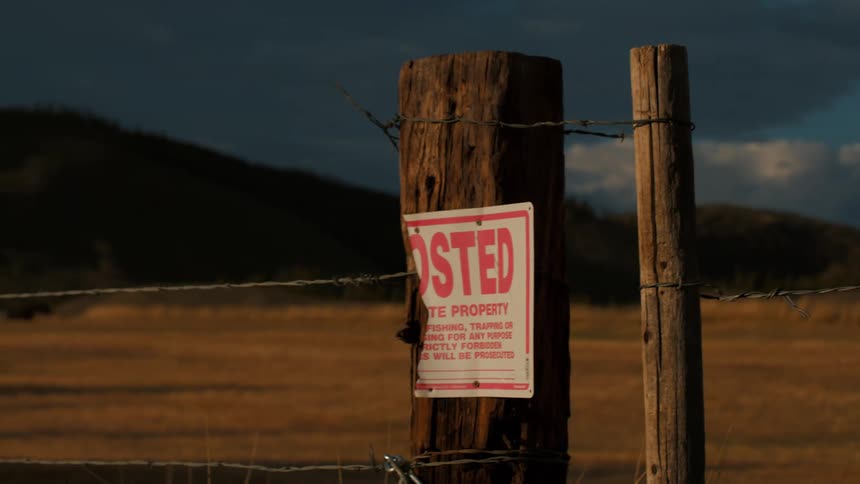 The image shows two horizontal lines of barbed wire stretched across the foreground these lines are made of twisted metal strands with sharp pointed barbs attached at regular intervalsthe wire is weathered and appears aged cutting across