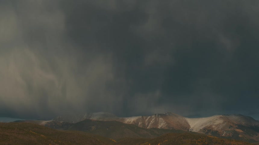 Dark gray clouds fill the sky above a snow covered mountain range